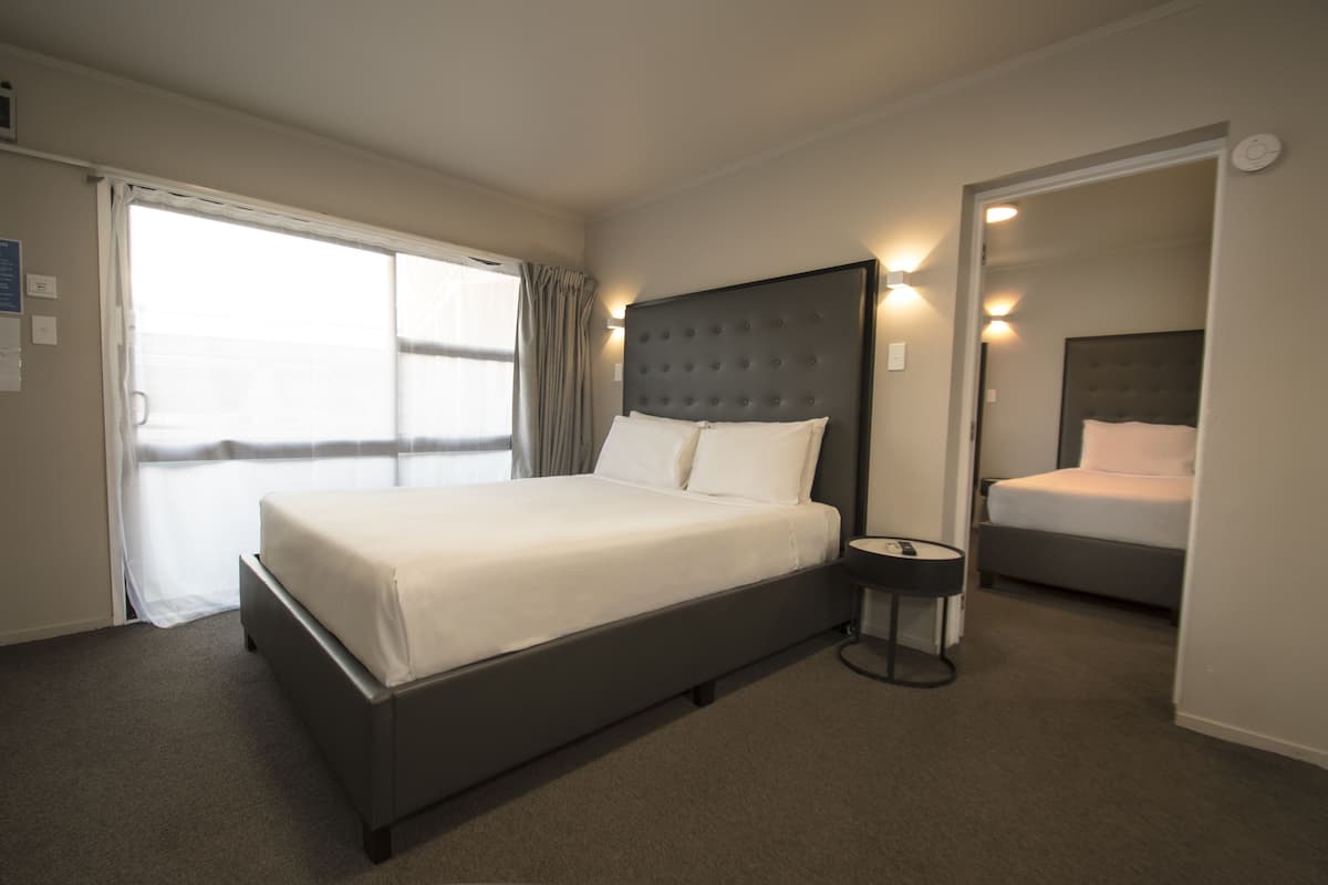 A modern hotel room with a large bed, a bedside table, and a view through a sliding door.