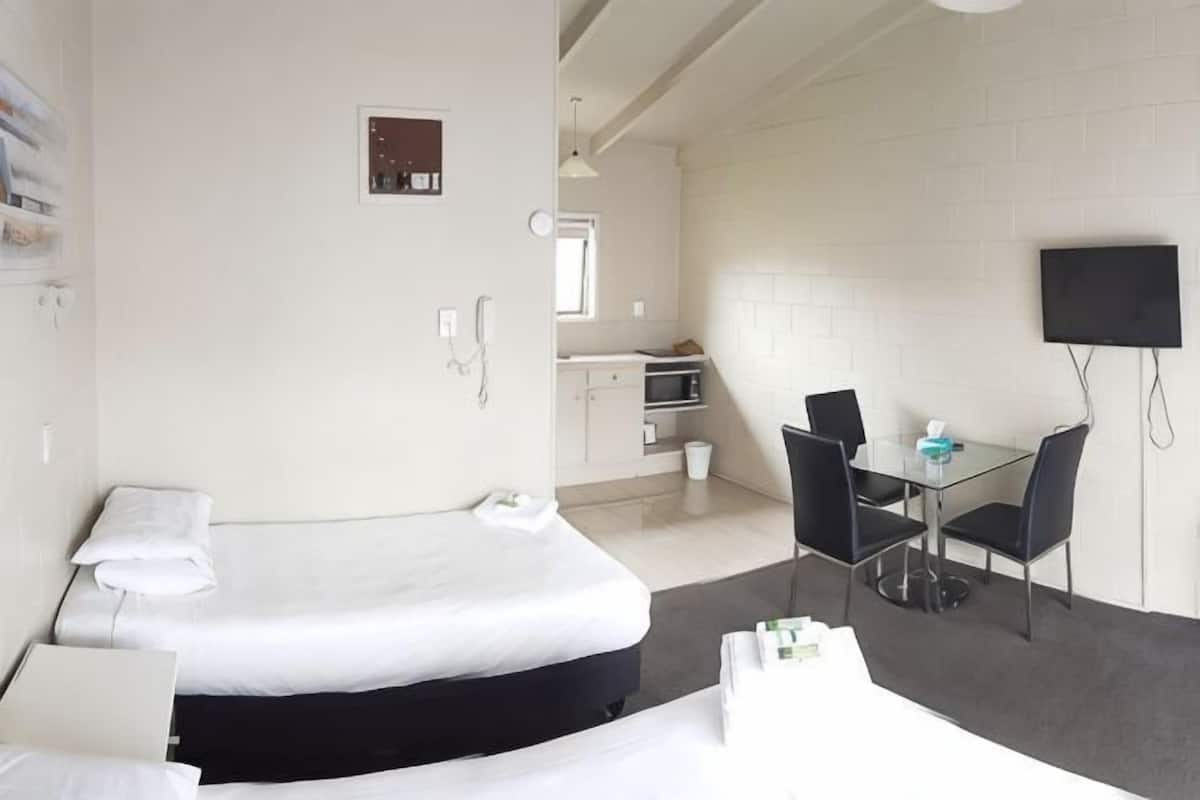 A hotel room with two beds, a desk, a chair, a TV, a microwave, and a small kitchenette.