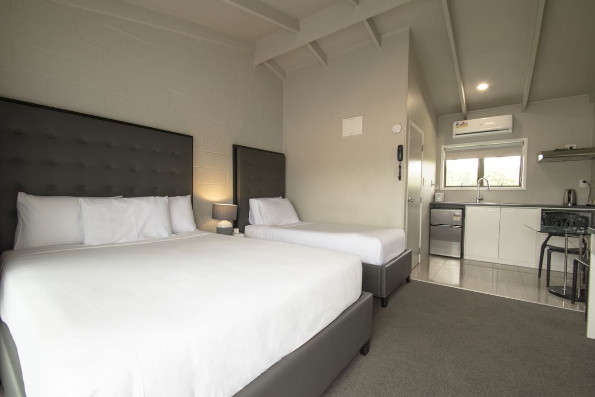 A hotel room with two beds, a kitchenette, and a bathroom.
