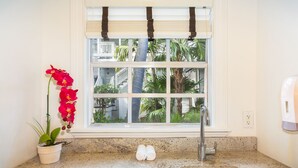 Cocina con encimera de granito, pileta blanca y ventana con vista a palmeras y un balcón.