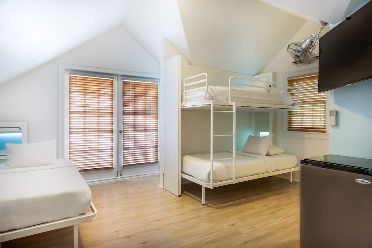 A dorm-style room with bunk beds, a bed, a refrigerator, and a ceiling fan.