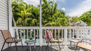 Una terraza de madera con dos sillas y una mesita, rodeada de exuberante follaje tropical.
