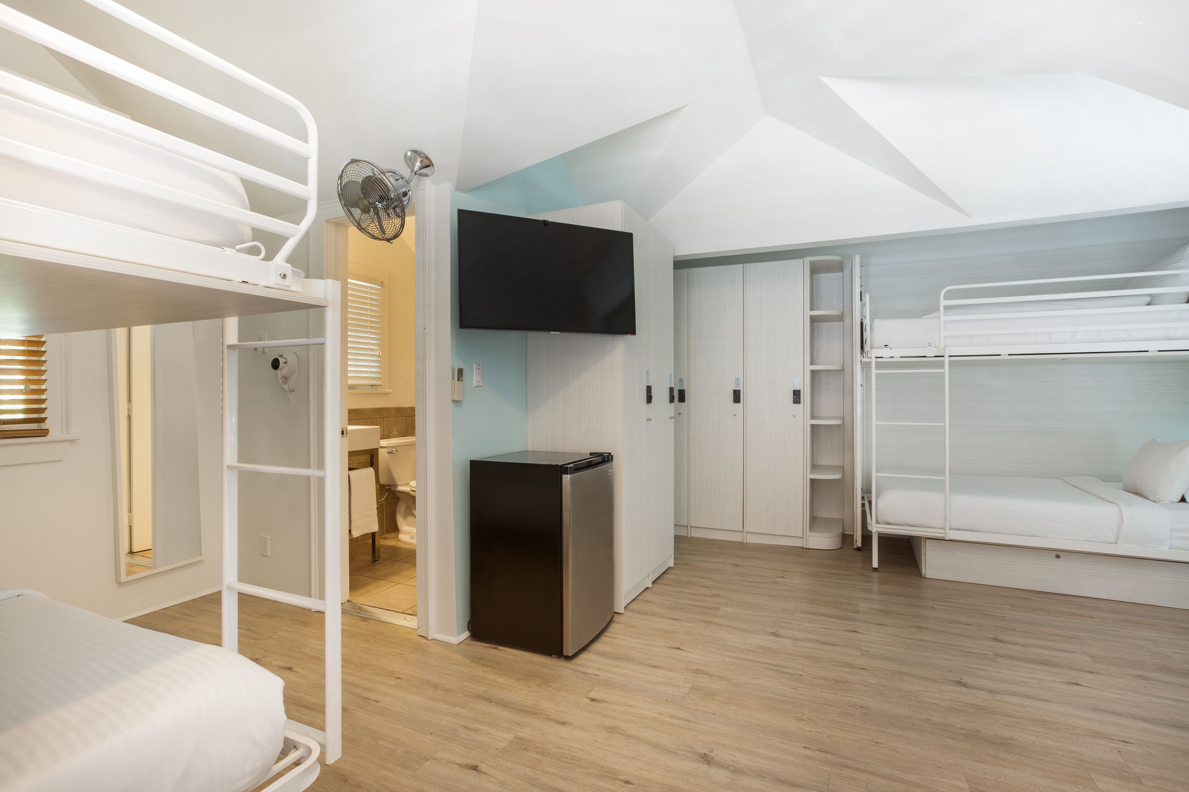 Ein kleines Zimmer mit Stockbetten, einem kleinen Kühlschrank, einem an der Wand befestigten Fernseher und Holzboden.