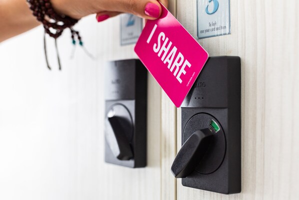A hand holding a pink card with "I SHARE" written on it, placed on a black card reader next to a door lock.