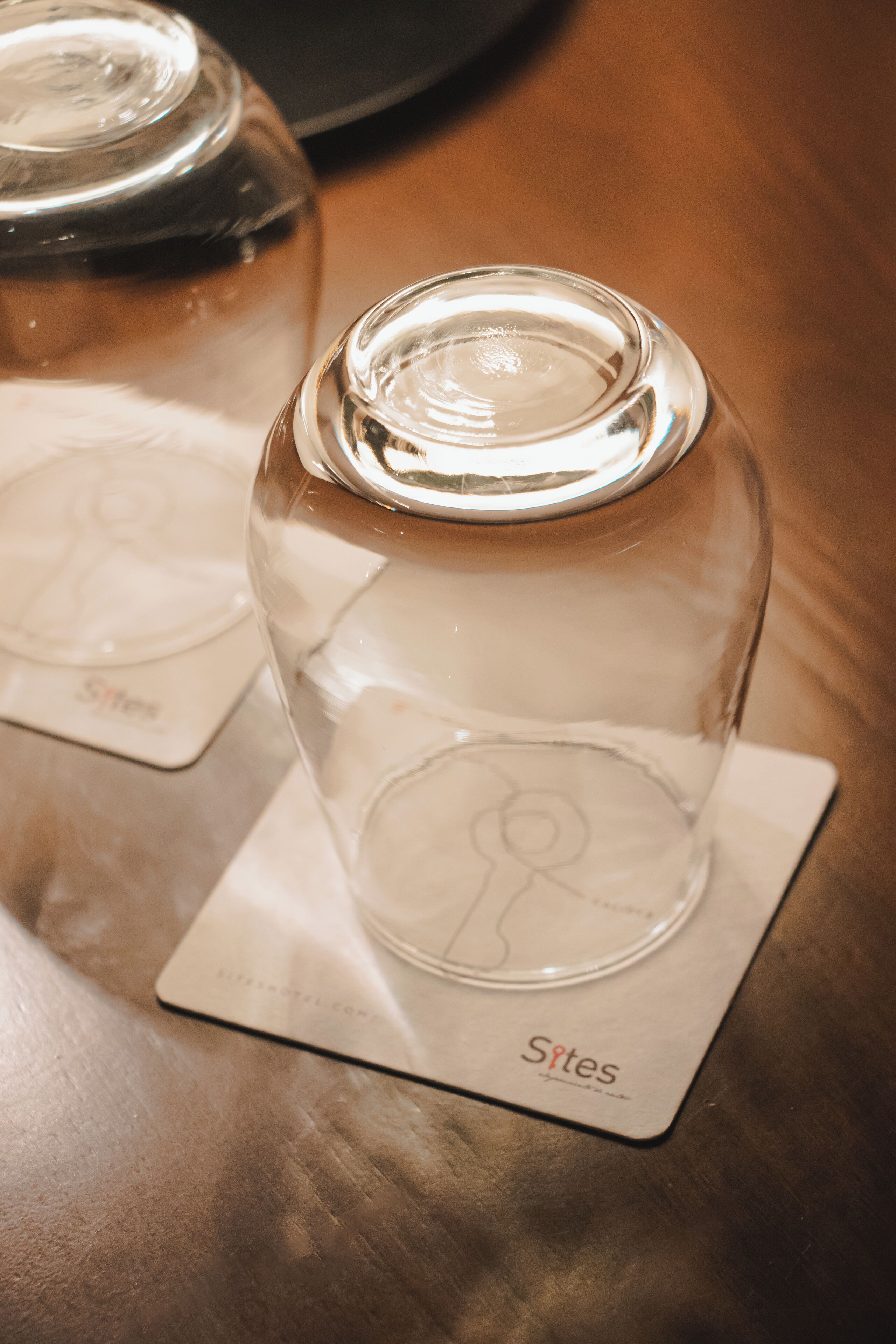 Un barattolo di vetro trasparente con un coperchio metallico su un tavolo di legno, insieme a un sottobicchiere con la scritta 'Sites'.