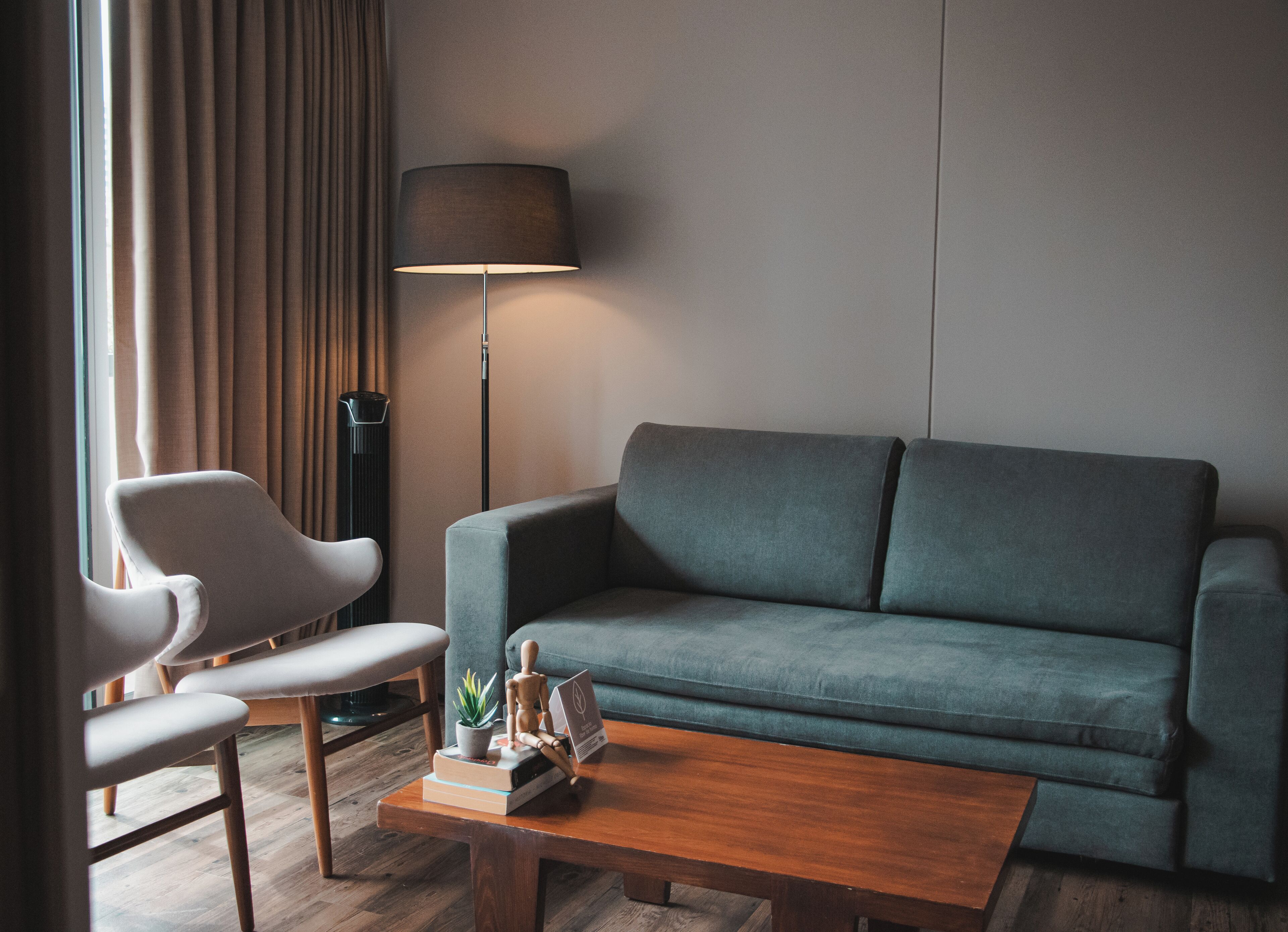A modern living room with a grey sofa, a wooden coffee table, and a white armchair. A floor lamp and a potted plant are also visible.