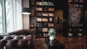 A cozy living room with a leather sofa, a bookshelf filled with books, a vase with flowers, and a large painting on the wall. - Sites Hotel (Medellín)