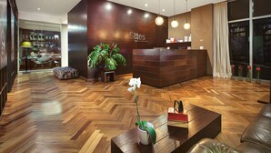 A modern hotel lobby with a reception desk, wooden flooring, a large potted plant, and a seating area with a coffee table and ottoman. - Sites Hotel (Medellín)