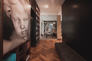 A hallway with a wooden herringbone floor, a large framed artwork on the left, and a seating area on the right. - Sites Hotel (Medellín)