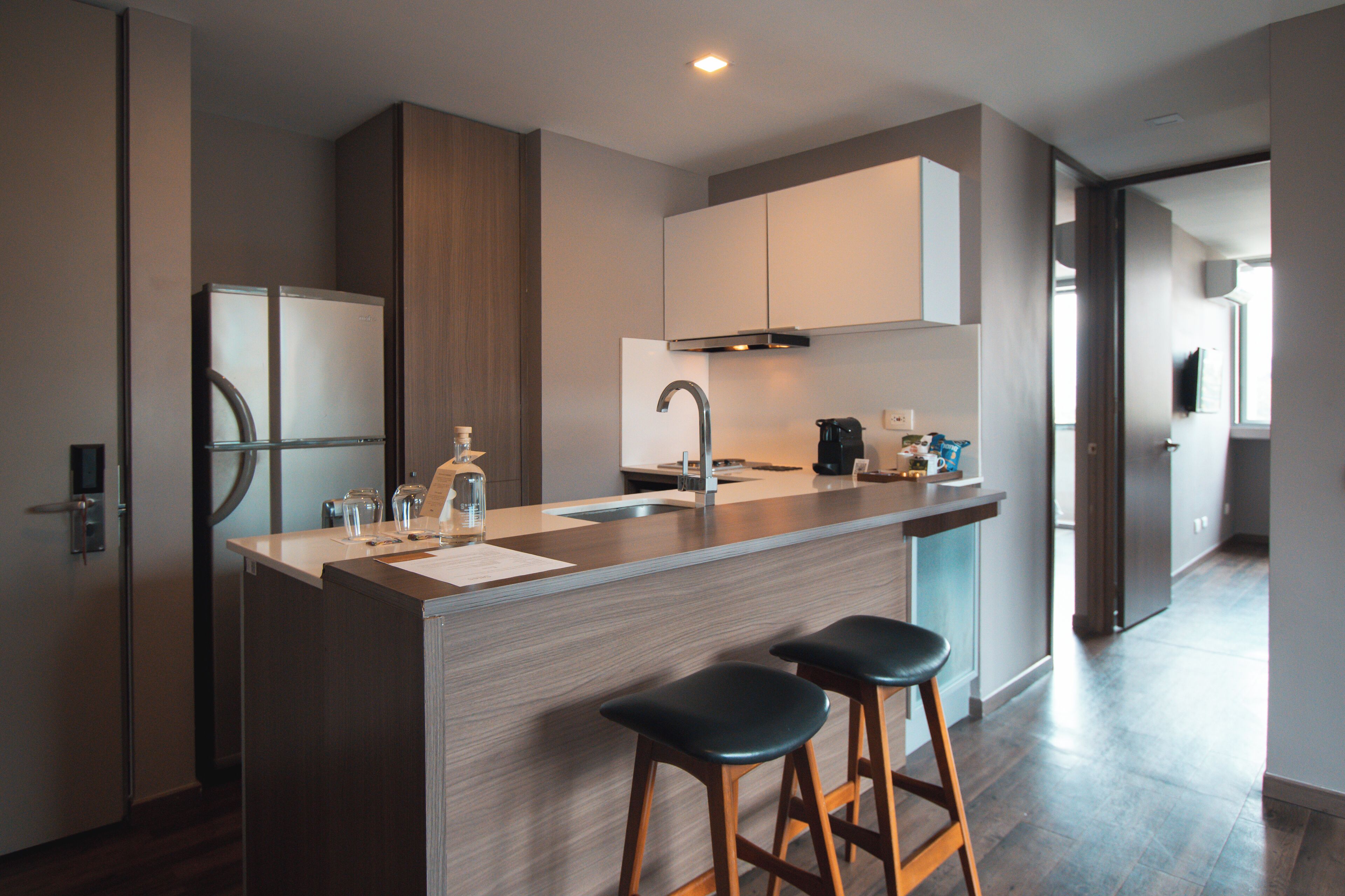 Una cocina moderna con una isla central, electrodomésticos de acero inoxidable, taburetes de bar de madera y vistas al área de estar contigua.
