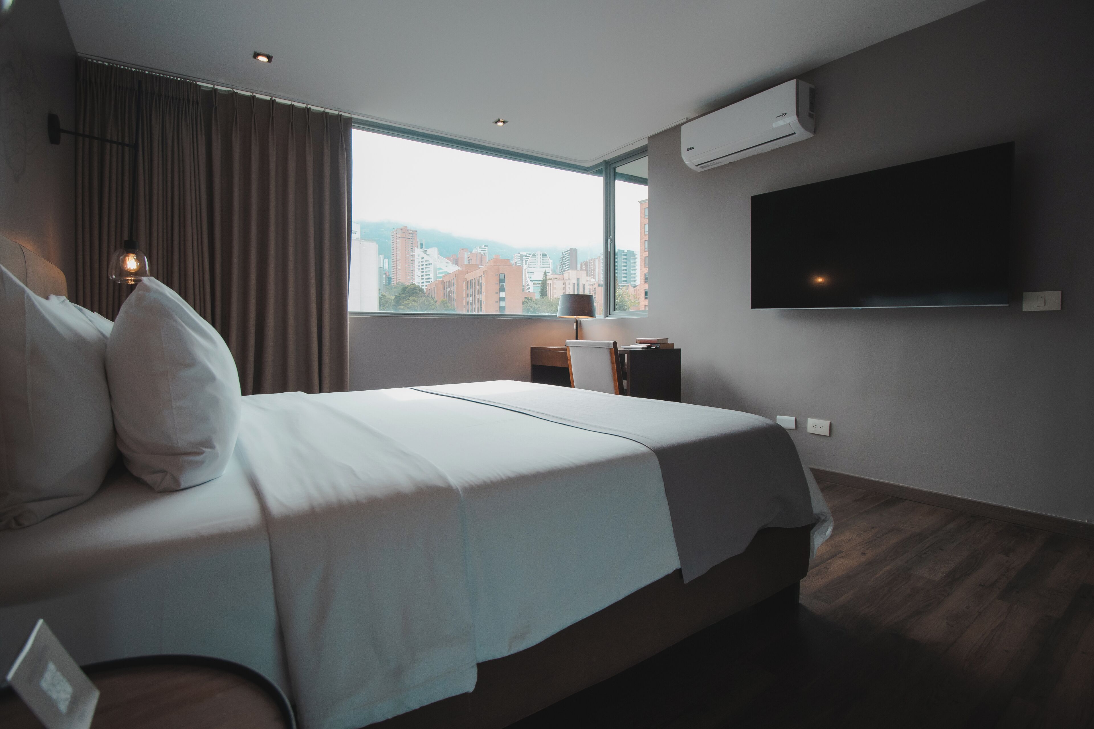 Camera d'albergo moderna con un ampio letto, una TV a schermo piatto, condizionatore d'aria e vista sulla città.