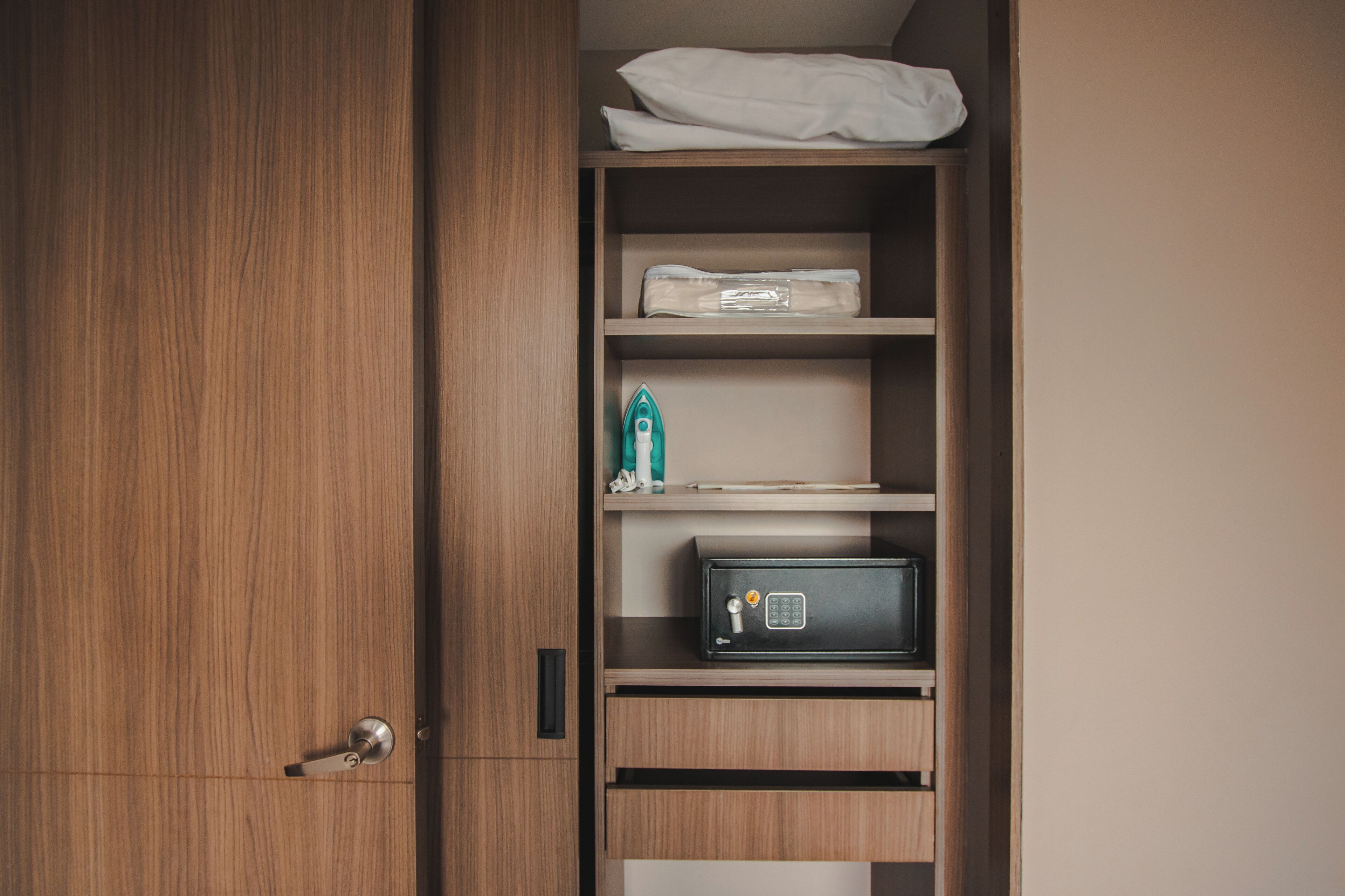 A wooden wardrobe with a combination lock, a small safe, and neatly folded clothes on shelves.