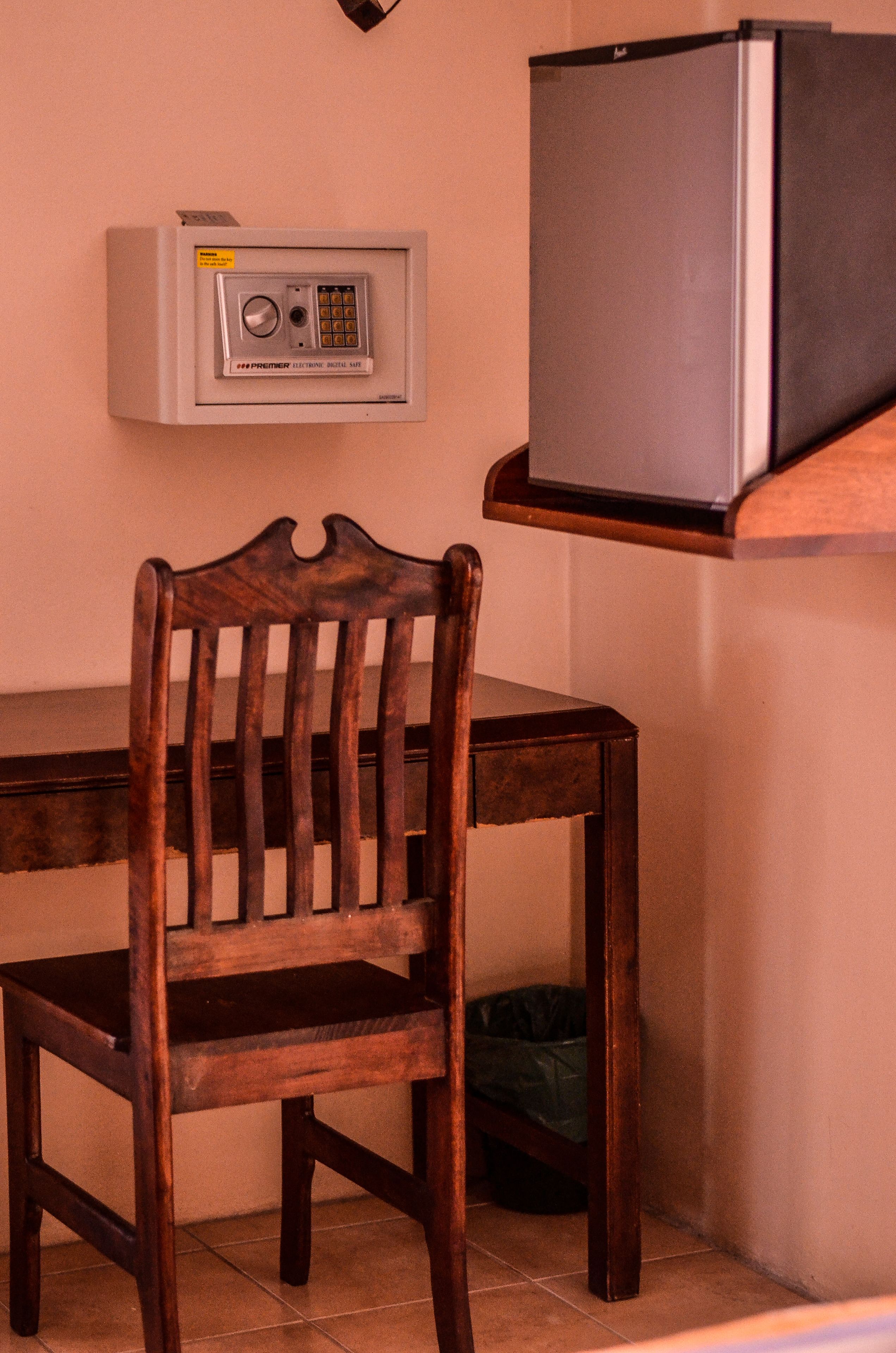 Una silla de madera, una mesita pequeña, una caja fuerte anclada a la pared y un televisor sobre una estantería.