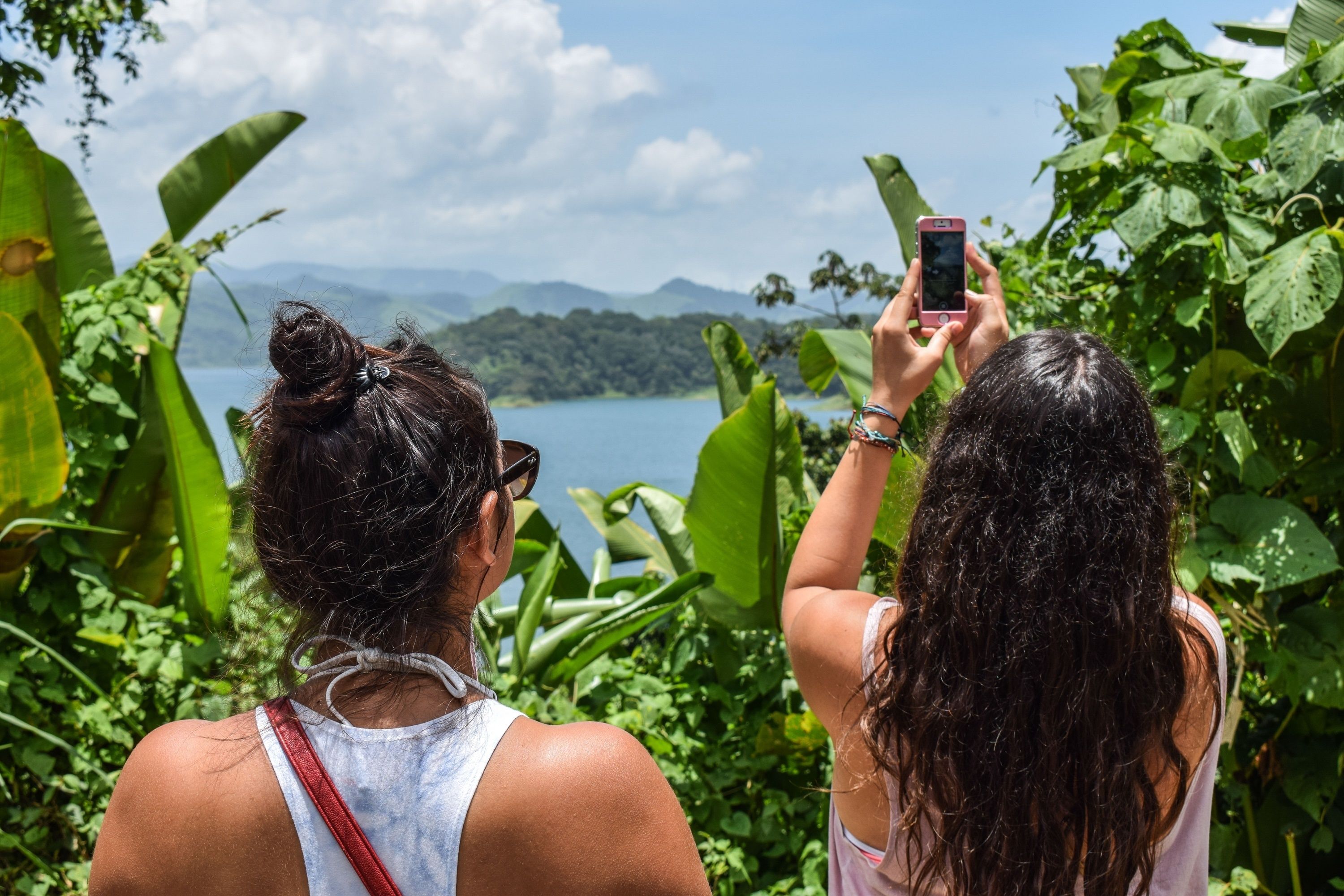 Two people taking a photo with a smartphone, surrounded by lush greenery and a lake view.