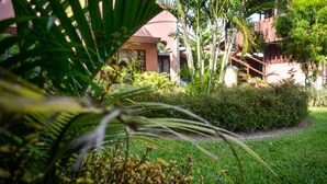 A lush garden with a pathway leading to a building with a red roof. - Hostel La Choza Inn (La Fortuna)