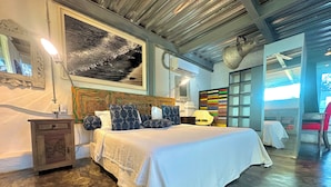 A modern bedroom with a large bed, a wooden nightstand, a mirror, and a colorful wall art piece.
