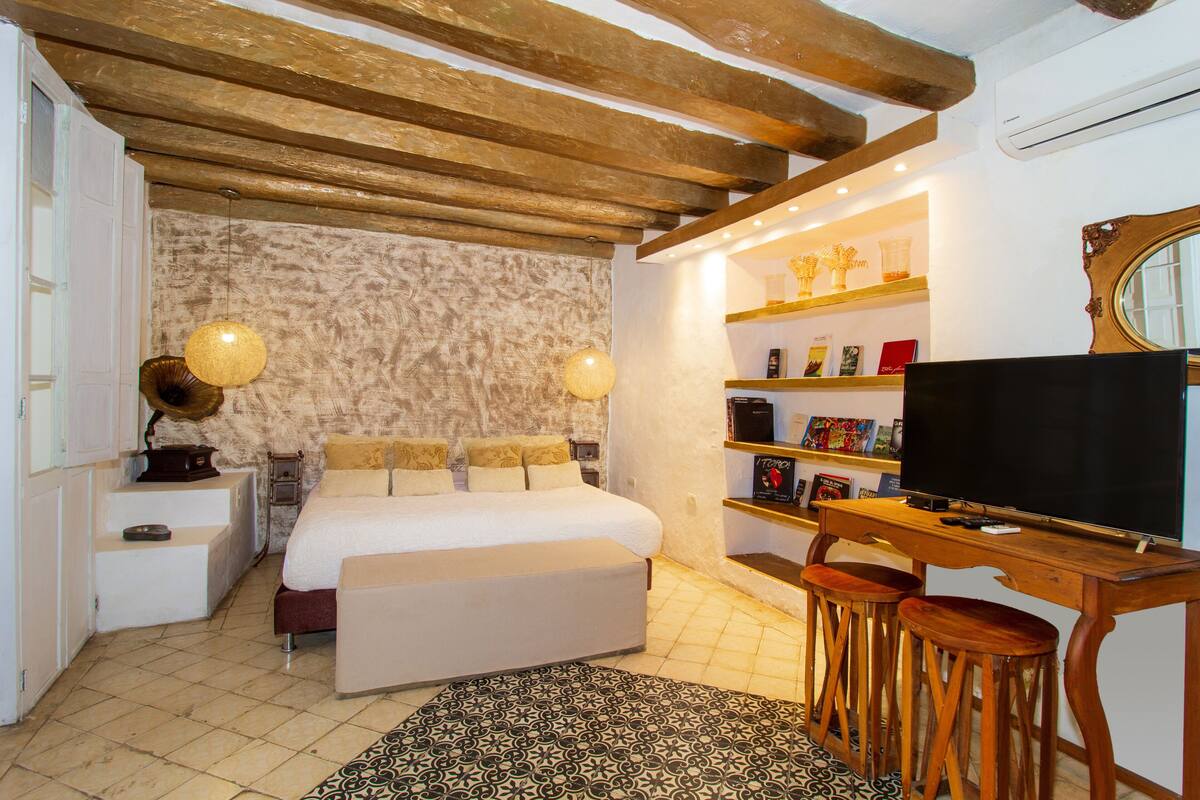 Een slaapkamer met een bed, nachtkastjes, een televisie en een boekenkast.