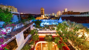 A rooftop garden with a checkered floor, a small pool, and a view of the city skyline including a tower.