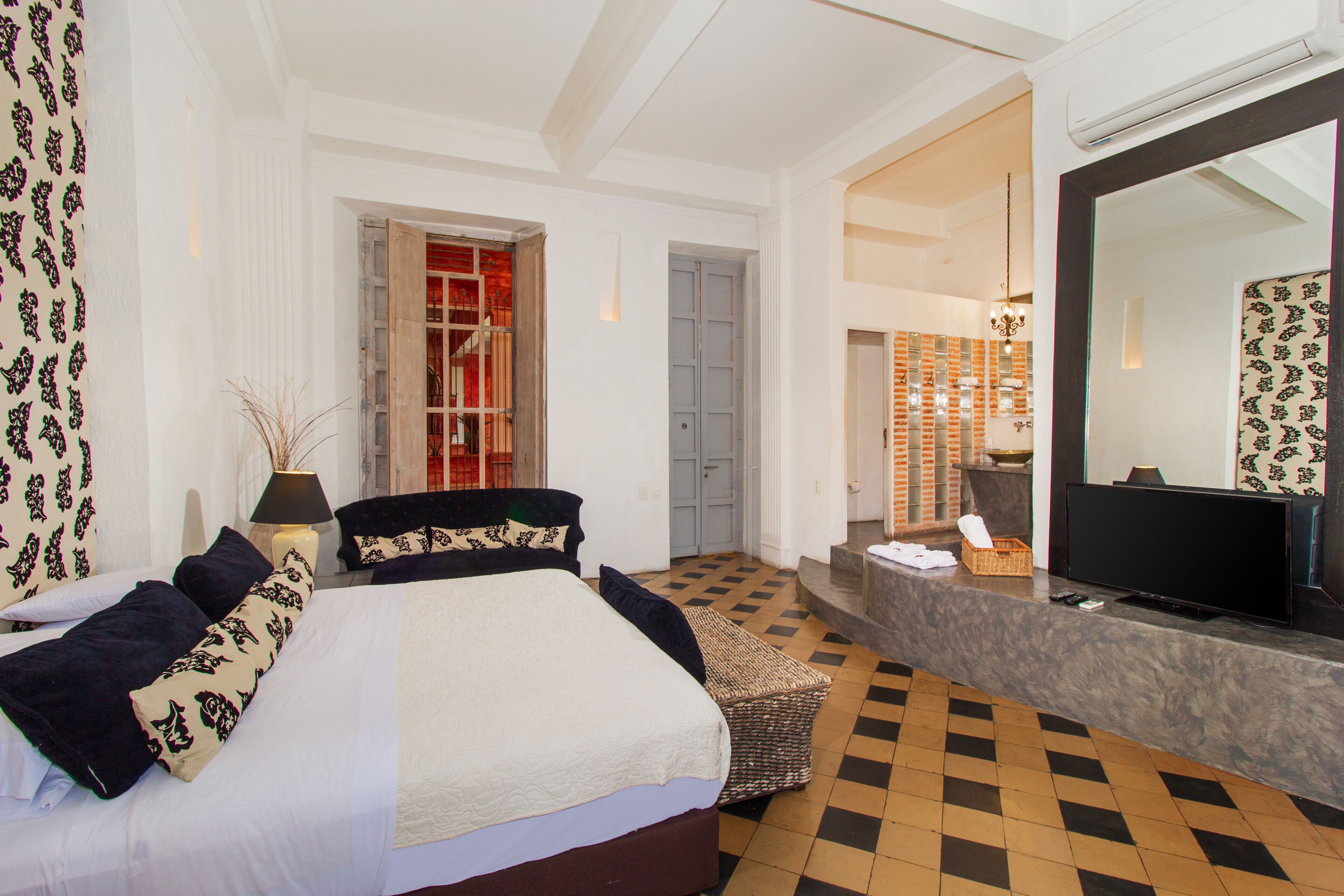 A hotel room with a large bed, a television, a desk, and a bathroom visible through an open door.