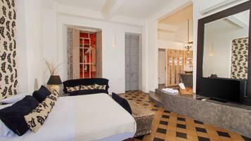 A hotel room with a large bed, a television, a desk, and a bathroom visible through an open door.