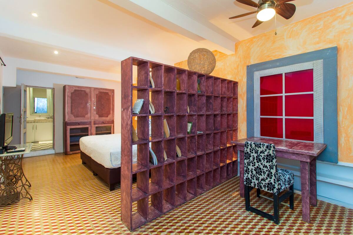 Een kamer met een bed, een bureau, een stoel, een boekenkast en een raam met rode ruiten.