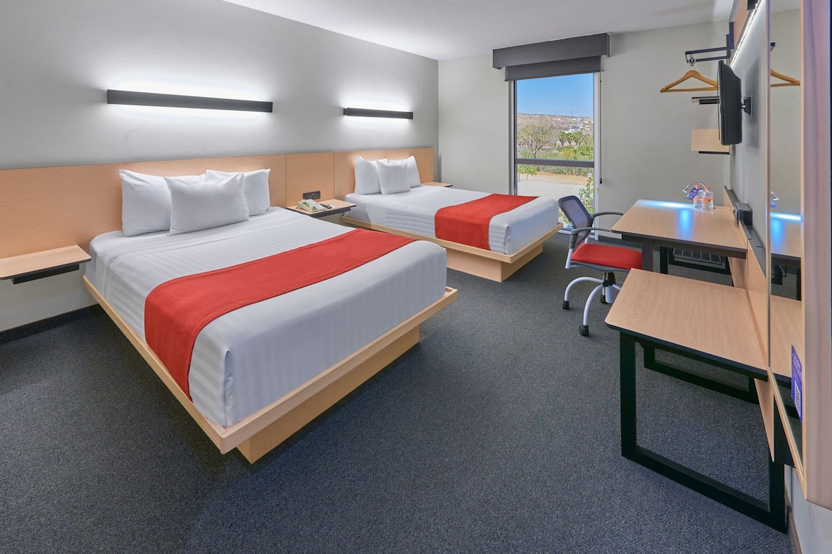 A hotel room with two beds, a desk, a chair, a TV, and a window with a view.