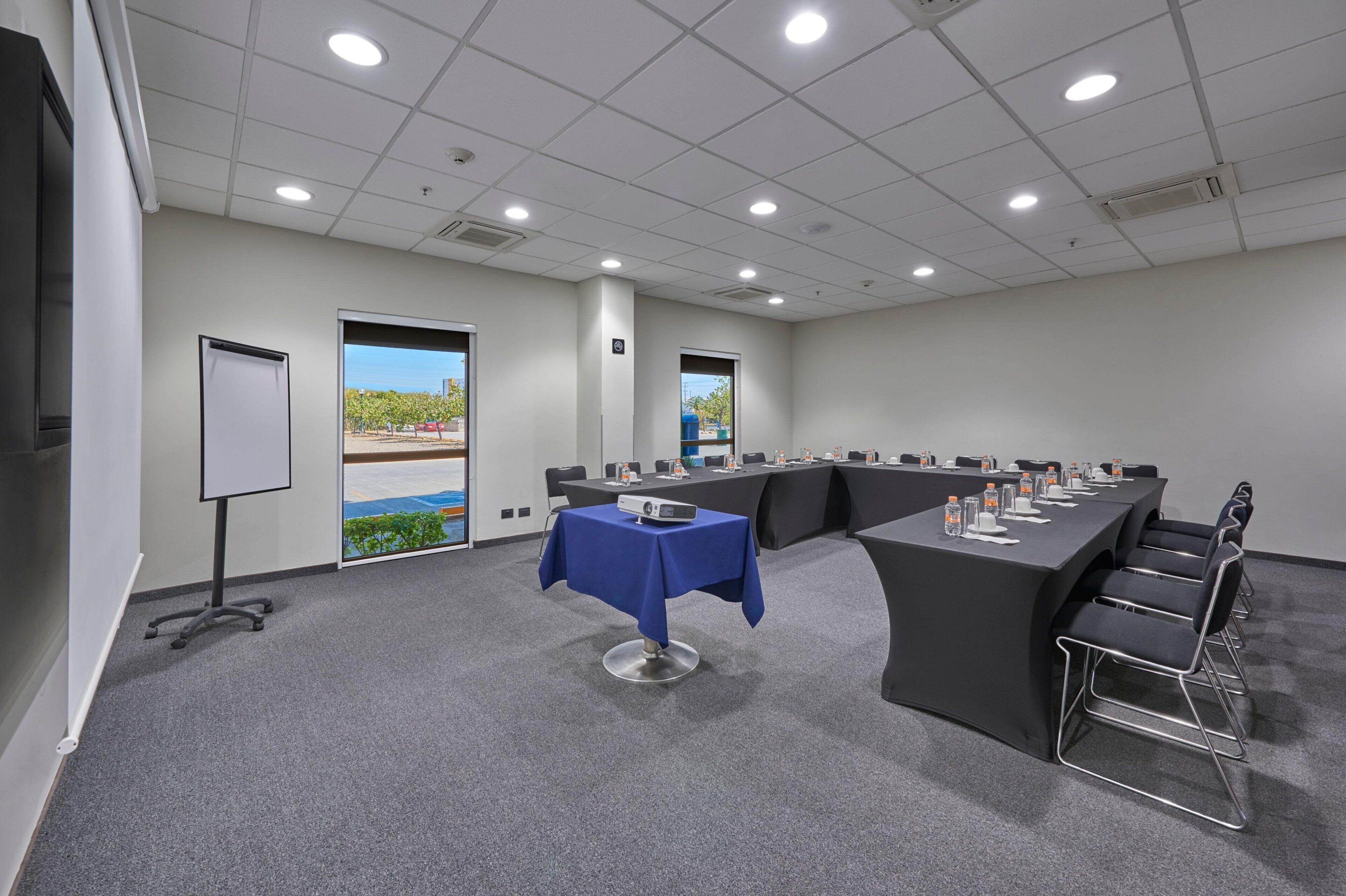 Un salón de conferencias con una mesa larga, sillas, un proyector y una pizarra.