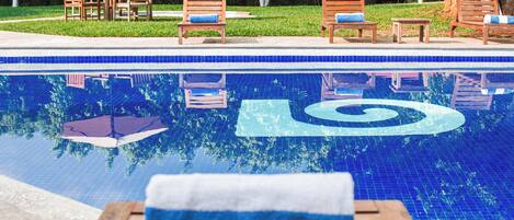 A pool with a blue tiled border and a spiral design, surrounded by wooden lounge chairs and a table with a towel.