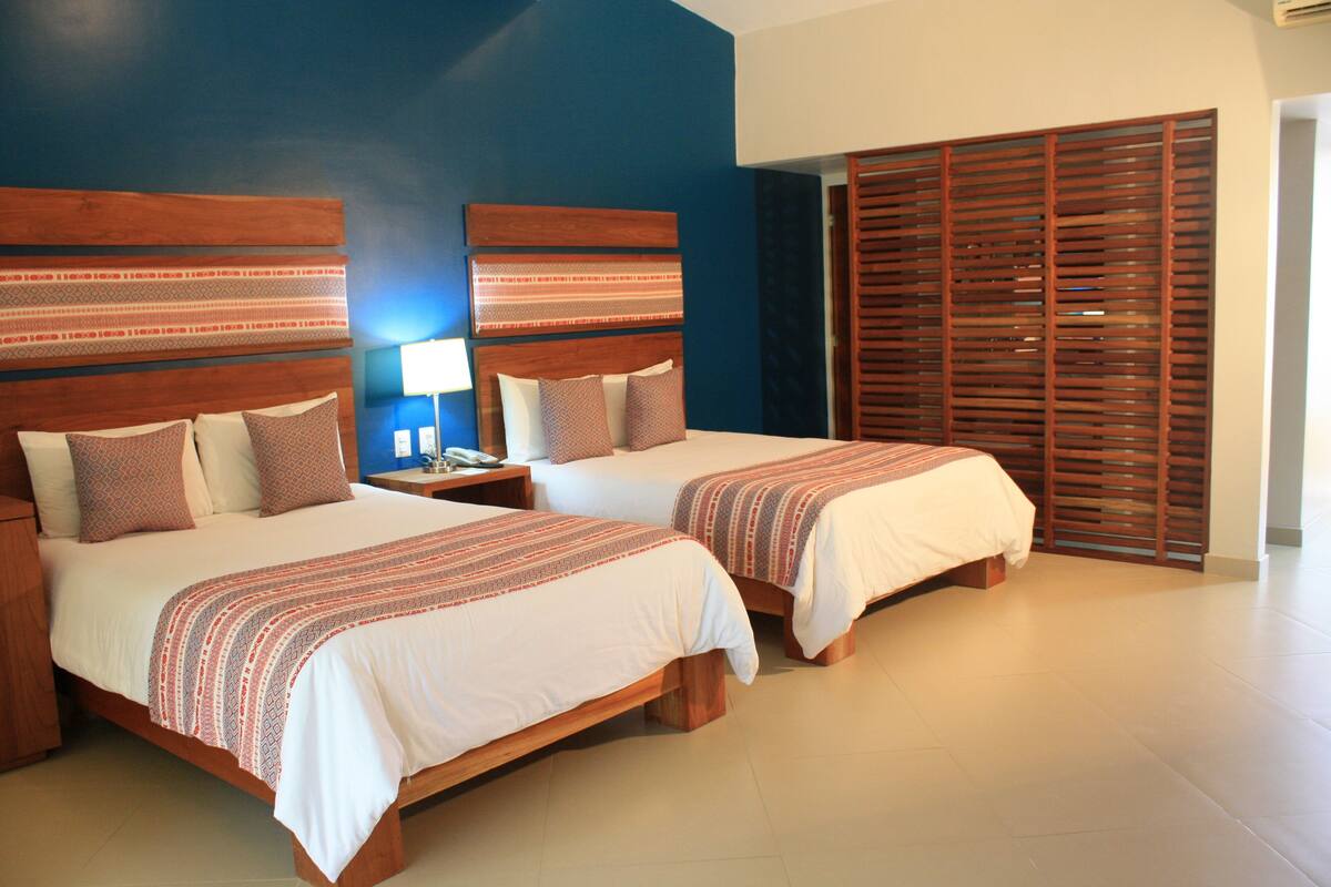 A hotel room with two beds, wooden headboards, and a large window with blinds.