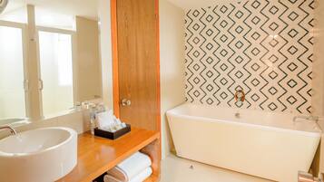 A bathroom with a wooden vanity, a white sink, a bathtub, and patterned wall tiles.