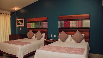 Habitación de hotel con dos camas, cada una con cabecero de madera, ropa de cama blanca y una manta con rayas rojas. Entre las camas hay una mesita de noche con un teléfono y una lámpara.