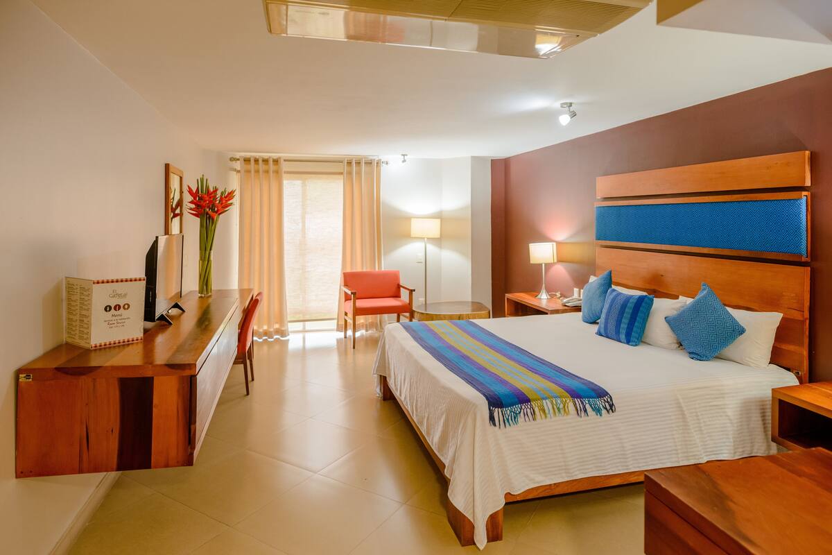 A hotel room with a bed, a desk, a chair, a lamp, and a window with curtains.