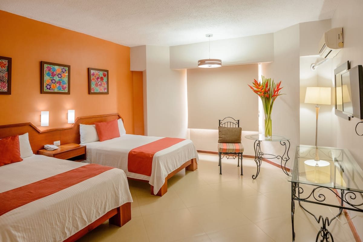 A hotel room with two beds, a sitting area with a chair and table, and artwork on the walls.