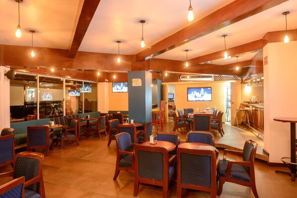 A restaurant with wooden tables and chairs, a bar area, and televisions displaying sports.