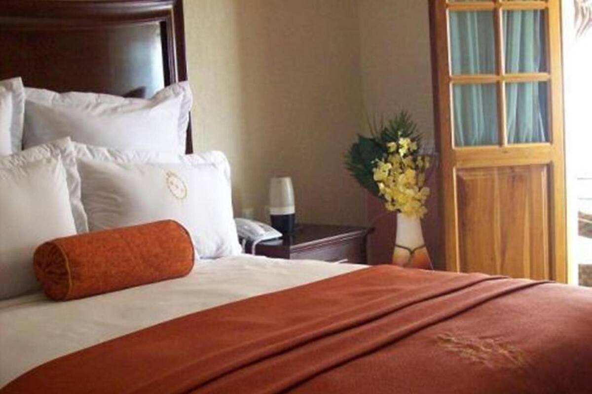 Une chambre d’hôtel avec un lit bien fait, une tête de lit en bois, une table de chevet avec une lampe et une fenêtre avec des rideaux.