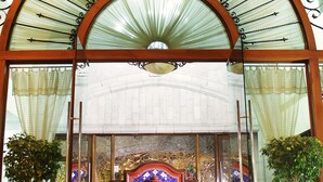 Un hall d’entrée doté d’une grande entrée en verre en arc de cercle, d’un sol carrelé et de deux plantes en pot.