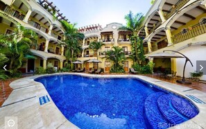 A pool area with a tiled swimming pool, surrounded by a multi-story building with balconies and outdoor seating. - Hacienda Real del Caribe (Playa del Carmen)