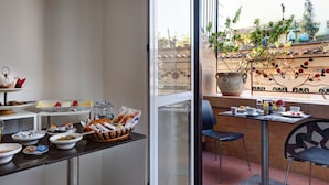 A breakfast buffet with various food items and a table with cups, plates, and a vase of flowers. - Little Rhome Suites (Rome)