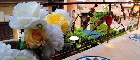 A balcony with a flower arrangement, a metal railing, and a tiled floor with a circular pattern.