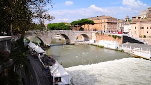 A river with a stone bridge, a boat dock, and buildings in the background. - Little Rhome Suites (Rome)