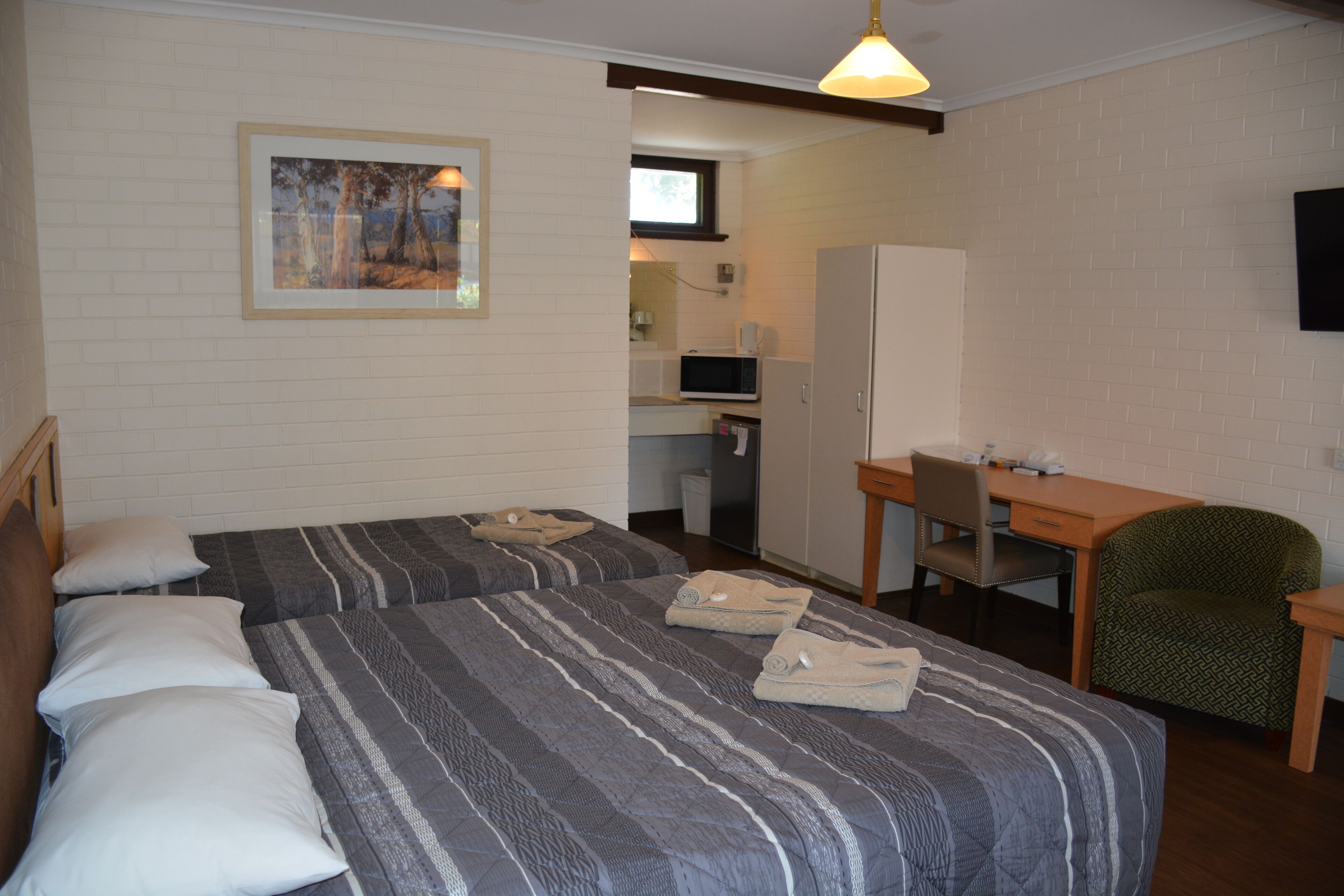 Habitación de hotel con dos camas, un escritorio, una silla y un televisor.
