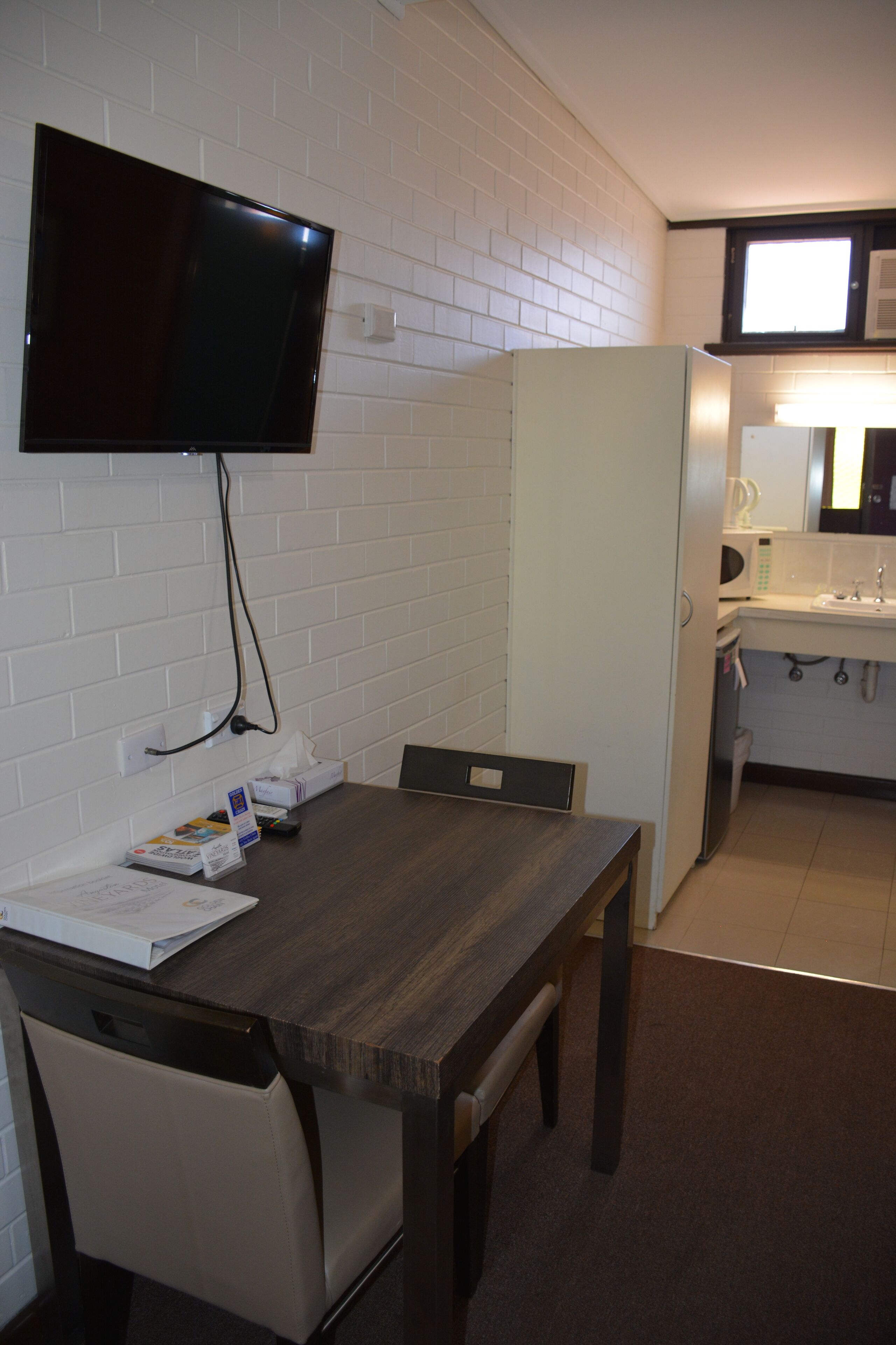 A compact kitchen with a microwave, sink, and a TV mounted on the wall.