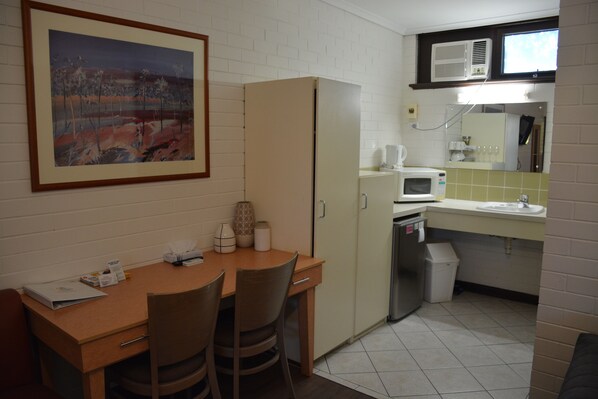 Una cocina compacta con una mesa de madera, sillas, un refrigerador, un microondas y un lavamanos.