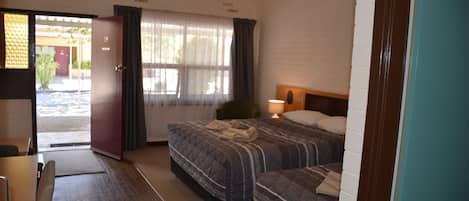 A hotel room with two beds, a desk, and a door leading outside.