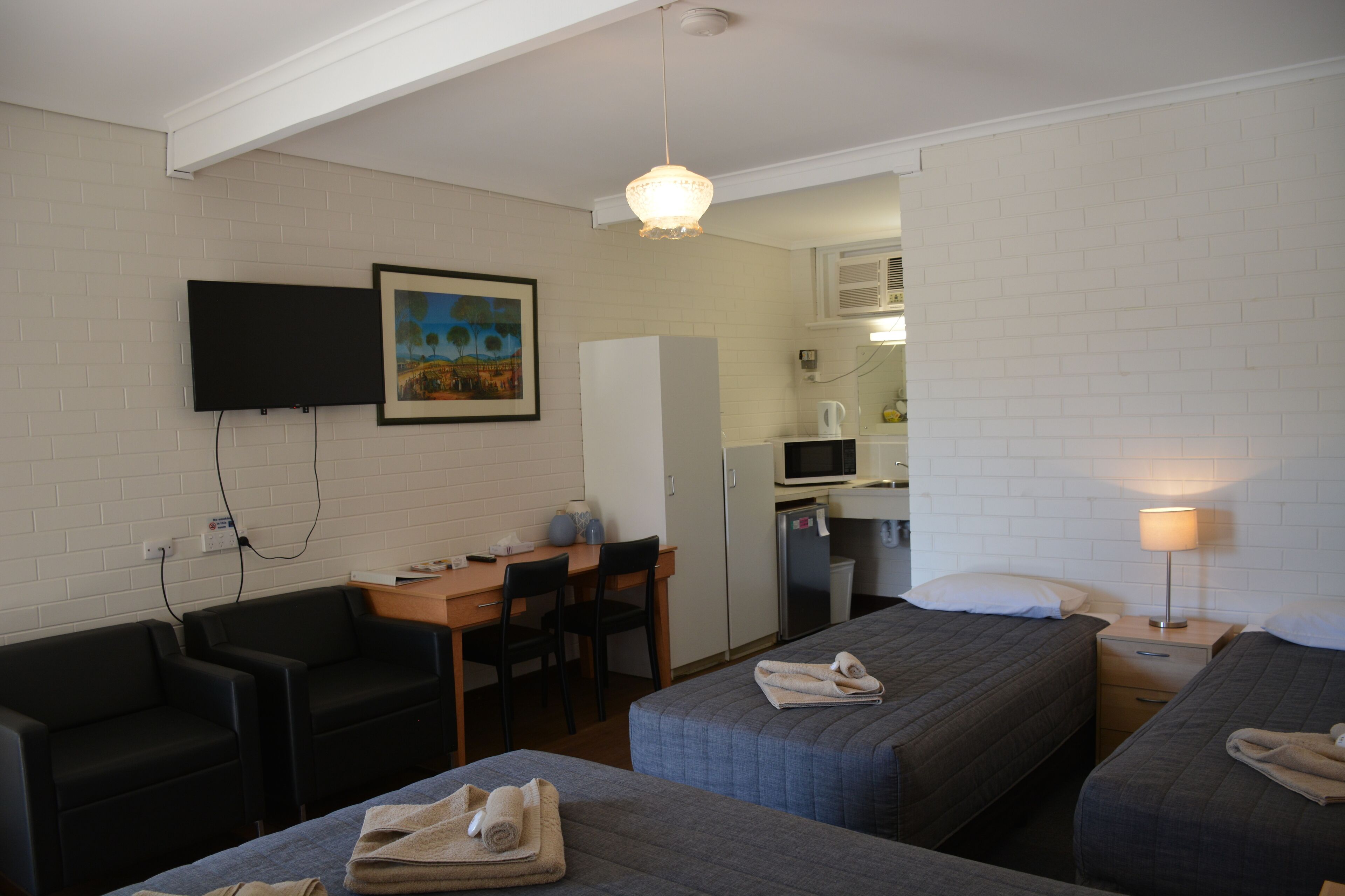 Une chambre d’hôtel avec deux lits, un bureau, une chaise, une télévision, un four à micro-ondes et une kitchenette.