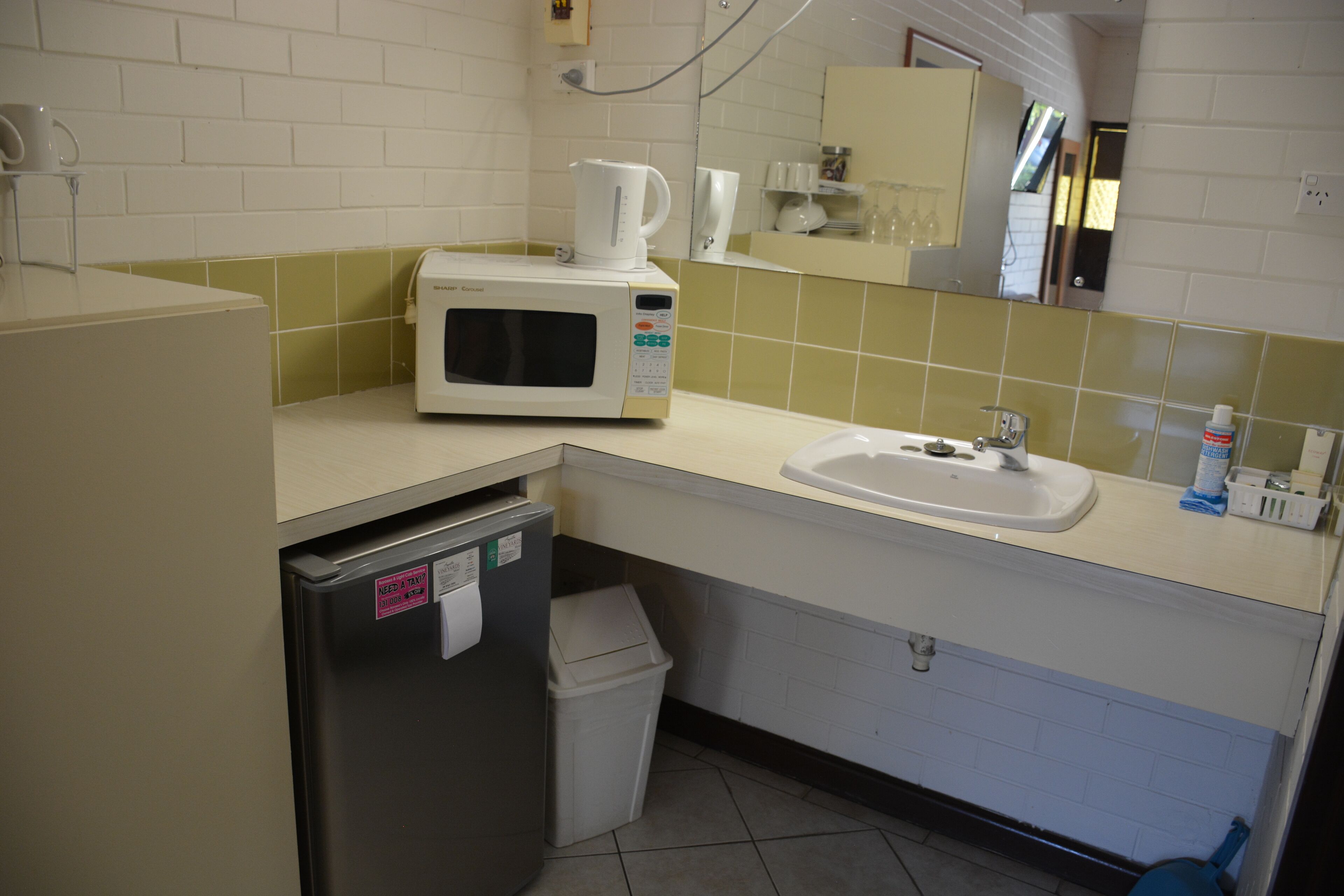 A small kitchenette with a microwave, sink, and trash bin.
