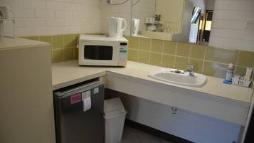 A small kitchenette with a microwave, sink, and trash bin.