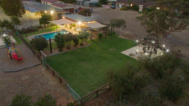 Vista aérea de una propiedad residencial con piscina, patio cercado e iluminación exterior.