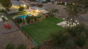 Vista aérea de una propiedad residencial con piscina, patio cercado e iluminación exterior.