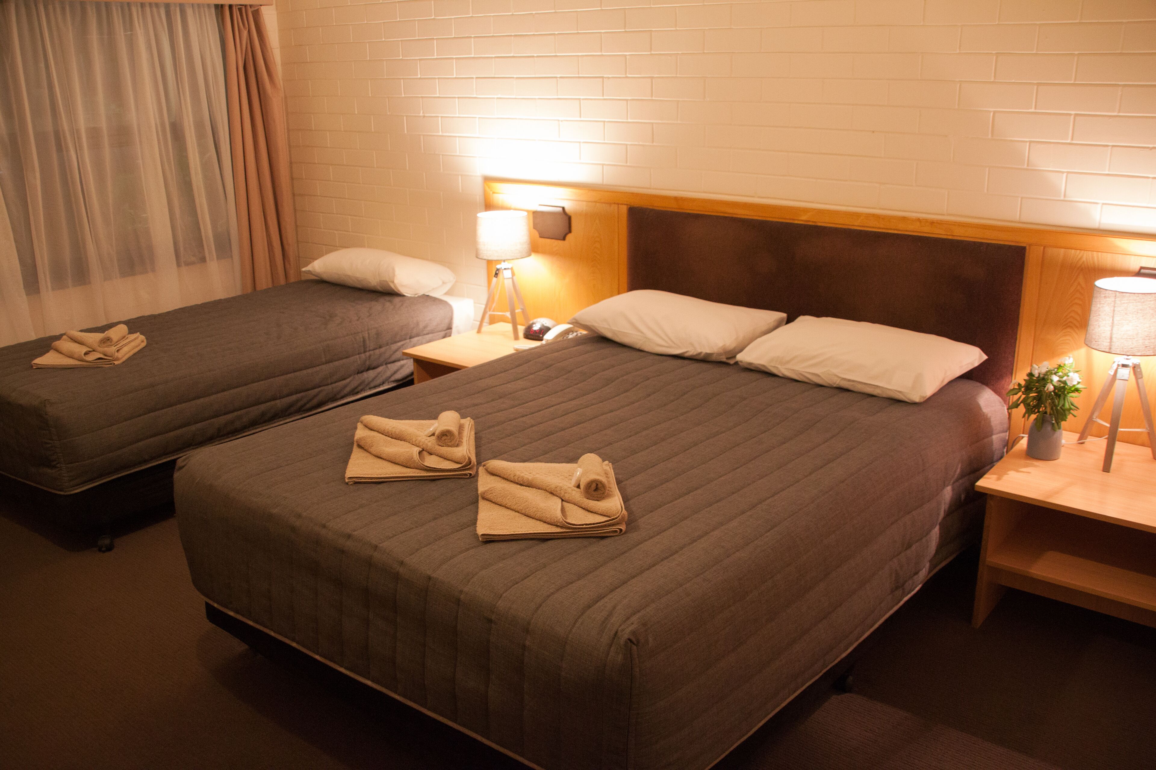 A hotel room with two single beds, each with a rolled towel, a bedside lamp, and a nightstand.